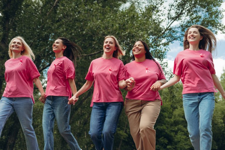 Women holding hands and wearing pink ribbon t-shirts running for breast cancer awareness